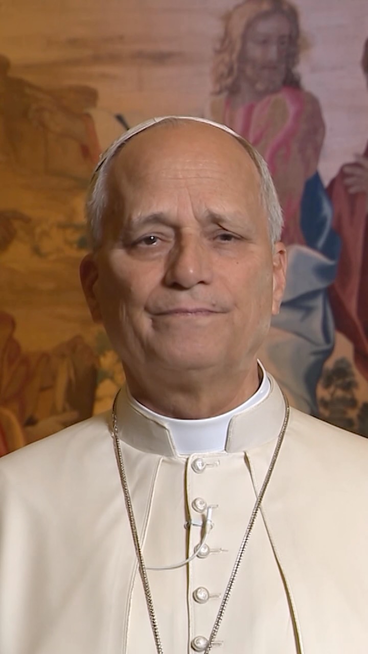 Close-up portrait of Pope Leo XIV speaking directly to camera with a warm classical religious painting behind him